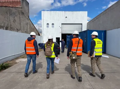 Cuatro profesionales con casco y chalecos de Higiene y Seguridad recorren el acceso de un establecimiento industrial