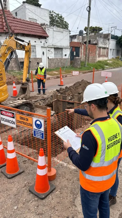 Dos profesionales de Higiene y Seguridad con planilla en mano revisan una excavación señalizada con vallado y carteles de peligro