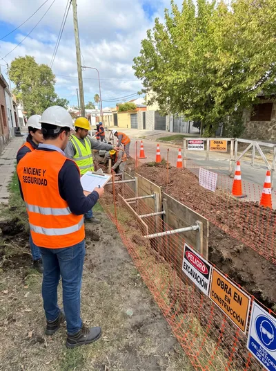 Profesional de Higiene y Seguridad controla con una planilla una zanja entibada y señalizada, mientras el personal trabaja